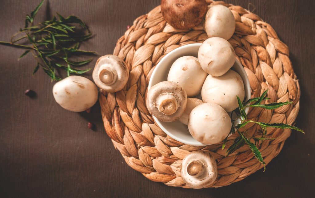 white button mushrooms in a white bowl on a brown braided table mat